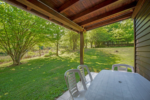 Vista dal lodge Manonfa in Belgio, terrazza con tavolo e sedie di plastica, prato e alberi verdi.