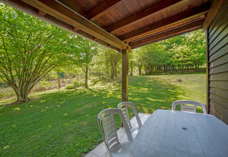 Vista dal lodge Manonfa in Belgio, terrazza con tavolo e sedie di plastica, prato e alberi verdi.