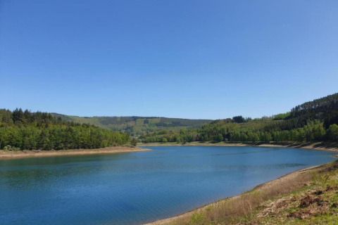 Vista di un lago tranquillo e colline boscose dal lodge Manonfa in Belgio in una giornata limpida.