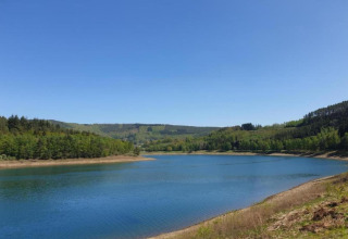Vista di un lago tranquillo e colline boscose dal lodge Manonfa in Belgio in una giornata limpida.