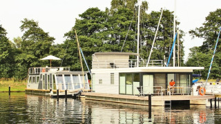 Due moderne houseboat, inclusa la Houseboat Xenia, ormeggiate presso un molo circondato da alberi verdi.