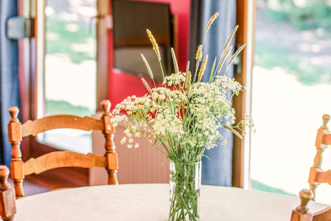 Veldbloemen in glazen vaas op een ronde tafel in lodge Manonfa in België met houten stoelen.