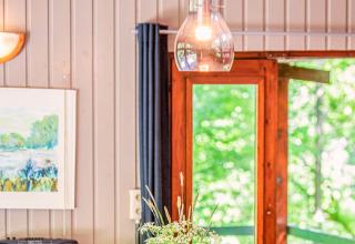 Binnenzicht van lodge Manonfa in België met houten wand, schilderij, lamp en zicht op het groen buiten.