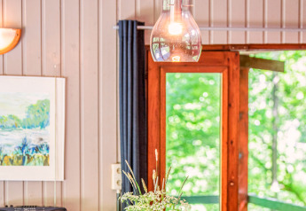 Immagine interna del lodge Manonfa in Belgio con lampada, pareti in legno e vista dalla finestra sul verde.