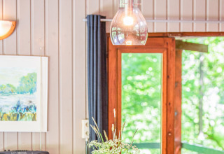 Immagine interna del lodge Manonfa in Belgio con lampada, pareti in legno e vista dalla finestra sul verde.
