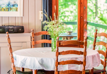 Tavolo rotondo con tovaglia bianca, sedie di legno e vaso di fiori selvatici alla lodge Manonfa in Belgio.