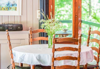 Tavolo rotondo con tovaglia bianca, sedie di legno e vaso di fiori selvatici alla lodge Manonfa in Belgio.