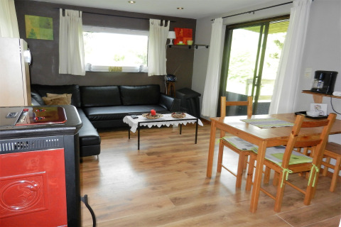 Stue i chalet Le Chaly i Belgien, med sort sofa, spisebord, træmøbler og store vinduer med udsigt.