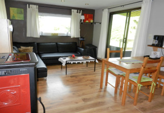 Stue i chalet Le Chaly i Belgien, med sort sofa, spisebord, træmøbler og store vinduer med udsigt.