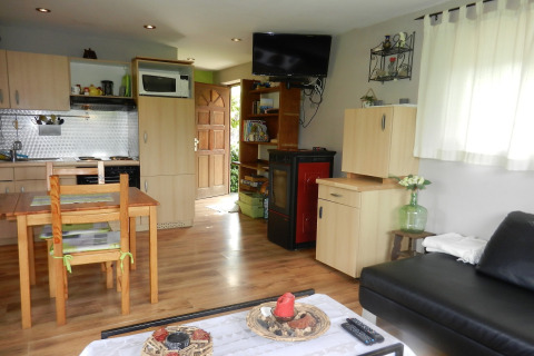 Stue og køkken i Le Chaly chalet i Belgien med træmøbler, sort sofa og tv på væggen.
