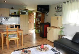 Stue og køkken i Le Chaly chalet i Belgien med træmøbler, sort sofa og tv på væggen.