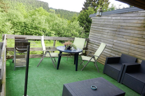 Udendørs terrasse på Le Chaly chalet i Belgien med kunstgræs, havemøbler og udsigt til skov.