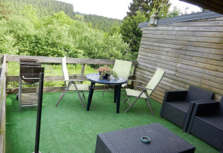 Udendørs terrasse på Le Chaly chalet i Belgien med kunstgræs, havemøbler og udsigt til skov.