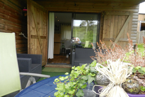 Udendørs terrasse ved træchalet 'Le Chaly' i Belgien med haveplanter og havemøbler foran en åben dør.