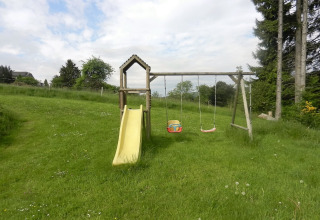 Legeplads med rutsjebane og gynger på grøn græsplæne ved chalet 'Le Chaly' i Belgien under blå himmel.