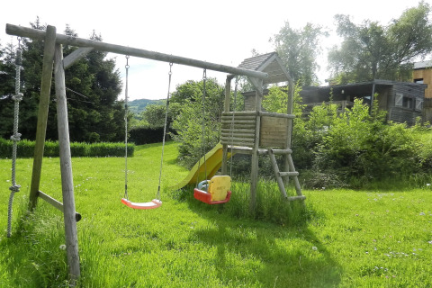 Legeplads ved chalet 'Le Chaly' i Belgien med gynger, rutsjebane og grønt græs under solen.