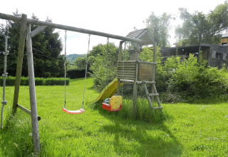 Legeplads ved chalet 'Le Chaly' i Belgien med gynger, rutsjebane og grønt græs under solen.