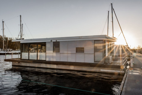 Moderne woonboot 475077 aangemeerd in een jachthaven bij zonsondergang, met zonnestralen op het water.
