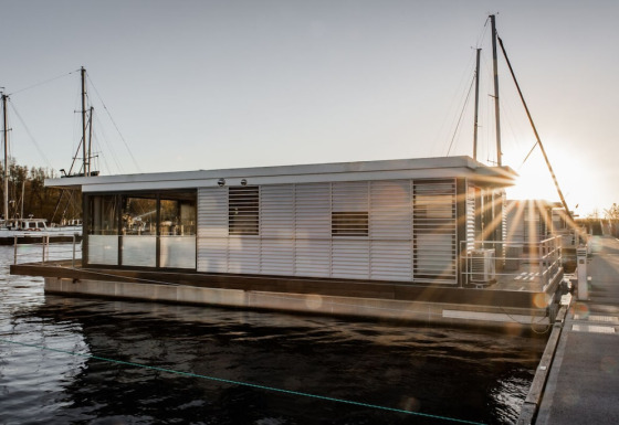 Moderne woonboot 475077 aangemeerd in een jachthaven bij zonsondergang, met zonnestralen op het water.