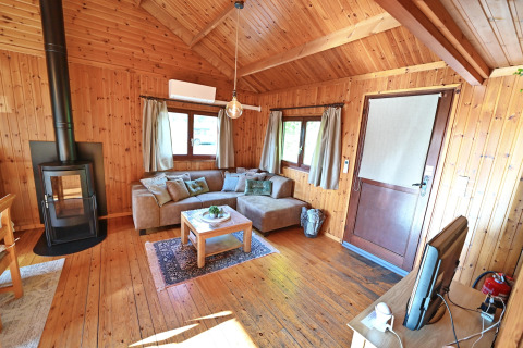 Woonkamer in chalet 'HORTENSIAS' in België met houten wanden, open haard, hoekbank en televisie.