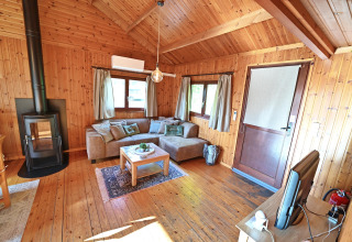 Woonkamer in chalet 'HORTENSIAS' in België met houten wanden, open haard, hoekbank en televisie.