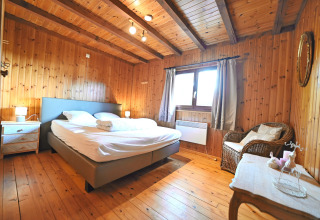 Gezellige slaapkamer met houten wanden, tweepersoonsbed en raam in chalet 'HORTENSIAS', België.