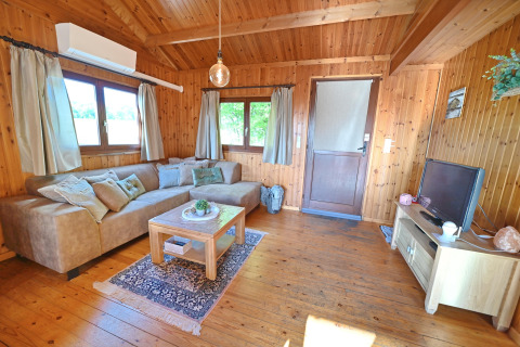 Gezellige woonkamer in chalet HORTENSIAS in België met houten inrichting, bank en televisie.