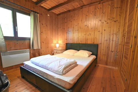 Slaapkamer in chalet «HORTENSIAS» in België met houten wanden, tweepersoonsbed en nachtkastlamp.