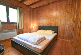 Slaapkamer in chalet «HORTENSIAS» in België met houten wanden, tweepersoonsbed en nachtkastlamp.