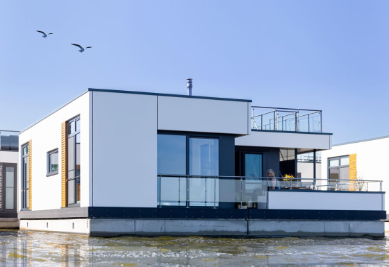 Casa flotante moderna con barandillas de cristal bajo un cielo azul en Ribnitz-Damgarten, Alemania.