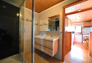 Moderne badkamer met houten plafond, dubbele wastafel en glazen douche in een chalet in België.
