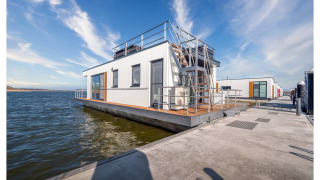 Moderne woonboot in Ribnitz-Damgarten met zonnig dakterras, aangemeerd aan een steiger langs het water.
