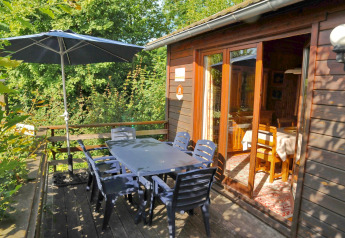 Terrasse extérieure à la lodge La Ribambelle en Belgique avec table, chaises, parasol et verdure luxuriante.