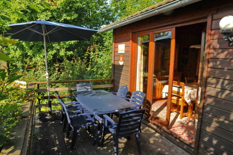 Udendørs terrasse ved La Ribambelle-lodge i Belgien med bord, stole, parasol og naturskøn udsigt.