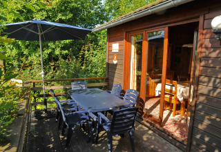 Udendørs terrasse ved La Ribambelle-lodge i Belgien med bord, stole, parasol og naturskøn udsigt.