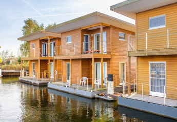 Moderne drijvende houten woningen met balkon, geschikt voor zes personen, aangemeerd aan het water.