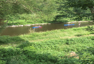Folk nyder en kano- og kajaktur på en flod omgivet af grøn natur ved et glampingsted om sommeren.
