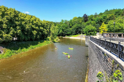 Vue d’un hébergement glamping sur une rivière avec des kayaks, bordée d’arbres et d’un mur de pierre.