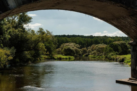 Uitzicht op een rustige rivier omgeven door groen, gezien onder een brug bij chalet HORTENSIAS in België.