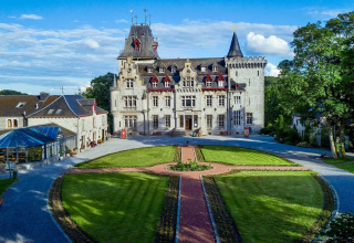 Et smukt slotlignende lodge, La Ribambelle, i Belgien, omgivet af velplejede haver under en blå himmel.