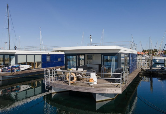 Foto de una casa flotante moderna con terraza amplia y paredes de cristal, atracada en un puerto deportivo.