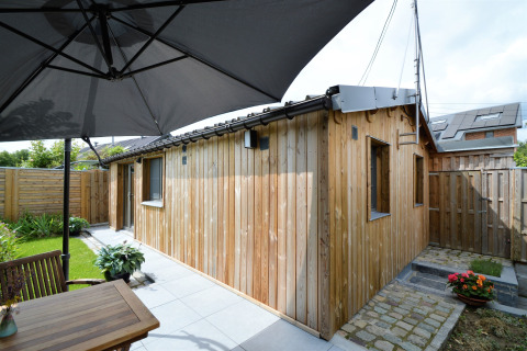 Terrasse extérieure au Chalet de Bioul avec façade boisée, mobilier de jardin et grand parasol.