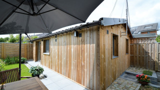 Patio exterior en Le Chalet de Bioul con cabaña de madera, muebles de jardín y gran parasol.