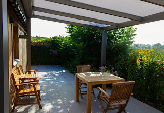 Terrasse extérieure du lodge Le Chalet de Bioul en Belgique, avec meubles en bois et verdure luxuriante.