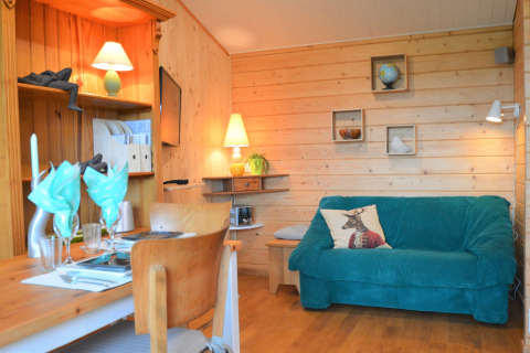 Chalet en bois chaleureux avec canapé bleu, table à manger et déco au Chalet de Bioul, Belgique.