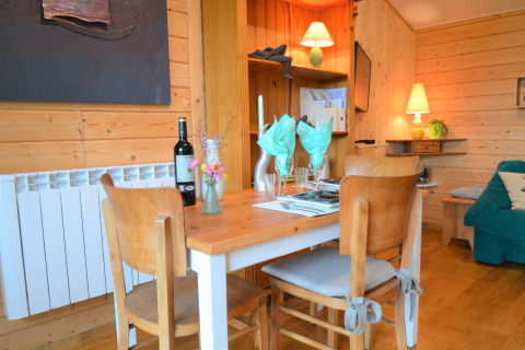 Salle à manger en bois avec table dressée, bouteille de vin et lumière chaleureuse au Chalet de Bioul, Belgique.
