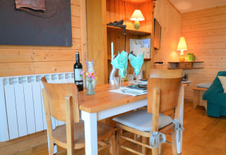 Salle à manger en bois avec table dressée, bouteille de vin et lumière chaleureuse au Chalet de Bioul, Belgique.