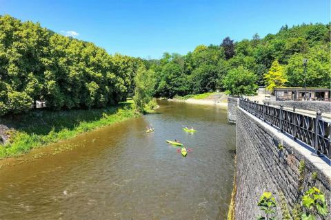 Kajakker på en flod ved Lodge La Ribambelle i Belgien, omgivet af frodige grønne træer og en stenmur.
