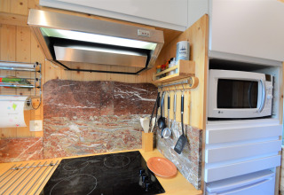 Coin cuisine moderne au Chalet de Bioul, Belgique, avec plaque, hotte, ustensiles et micro-ondes.