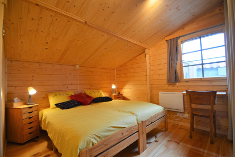 Chambre en bois au Chalet de Bioul en Belgique, lit double jaune, deux tables de chevet, bureau et fenêtre.